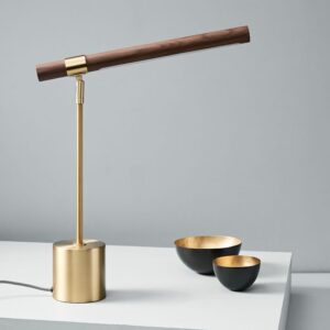 Sur une table blanche on voit à droite une lampe avec le pieds en métal doré et bois et à gauche de la table de petit bol noir à l'intérieur doré.