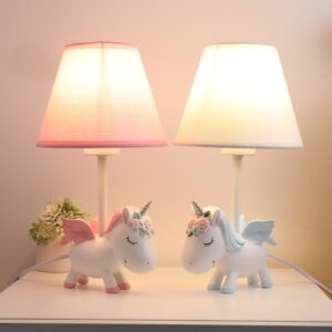 Sur une table blanche on voit deux lampes pour enfant en forme de licorne allumées. À droite une bleue et à gauche une rose.